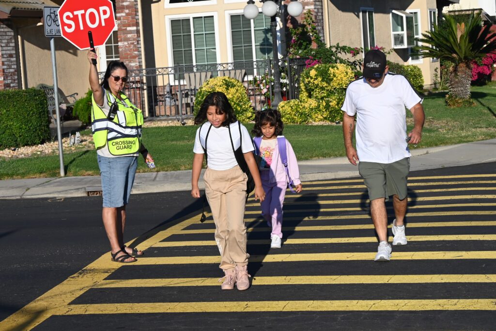 Children walking to school at a crosswalk with a crossing guard.